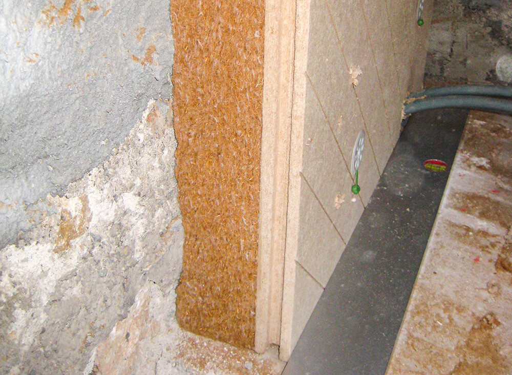 UdiIN RECO est un système d’isolation conçu pour rénover les parois verticales. Il repose sur une structure en deux couches combinant un panneau isolant rigide de 40 mm, destiné à recevoir un enduit, et un panneau isolant flexible en fibres de bois positionné côté support. Ce principe permet une adaptation aux irrégularités du mur grâce à un système de fixation spécifique, offrant une capacité de réglage d’environ ± 10 à 20 mm, variable selon l’épaisseur totale de l’isolation. Le système est compatible avec des supports minéraux solides ainsi qu’avec des structures en bois massif, ce qui élargit son champ d’application en rénovation. L’organisation en couches favorise une paroi ouverte à la diffusion de vapeur, tout en contribuant à l’atténuation des bruits et à une régulation hygrothermique de l’ambiance intérieure.
Adapté aux murs extérieurs et aux intérieurs